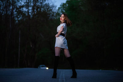 Full length of young woman standing against trees