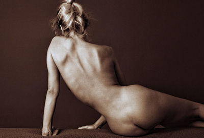 Rear view of naked woman sitting against wall