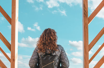 Rear view of mature woman with backpack standing against blue sky