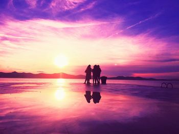 Silhouette people on beach against sky during sunset