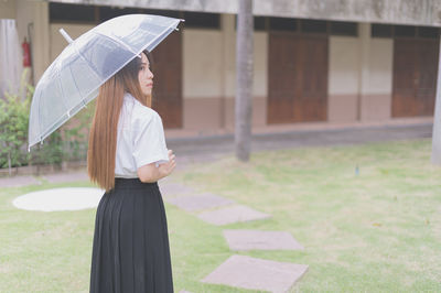 Woman with umbrella standing against built structure