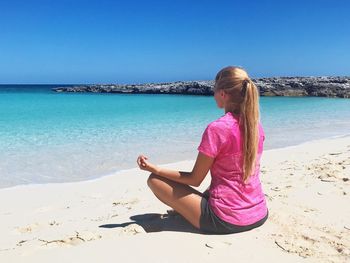 Woman sitting on beach by sea against sky