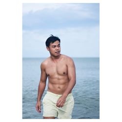 Full length of shirtless man standing in sea against sky