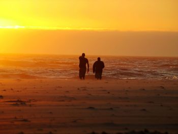 Silhouette men standing on beach against sky during sunset