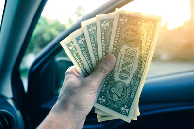 Cropped hand holding paper currencies in car