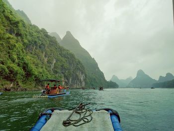 People on boats in sea against mountains