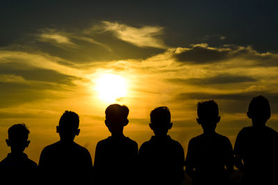 Rear view of silhouette boys standing against sky during sunset