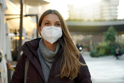 Portrait of young woman wearing medical face mask in city street as prevention against virus