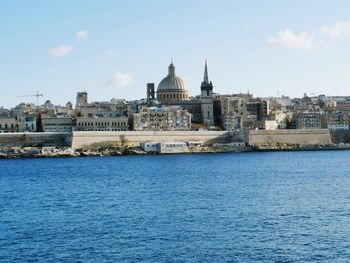 View of buildings by sea against sky in city