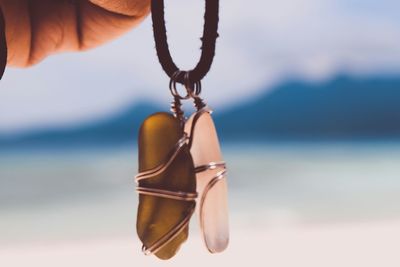 Cropped hand holding lockets against sea