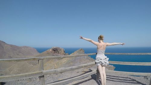 Rear view of woman standing by railing against clear blue sky