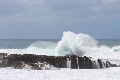Waves splashing on shore against sky