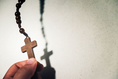 Cropped hand of person holding rosary against wall