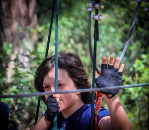 Thoughtful boy holding ropes against plants