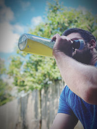 Close-up of man holding glass bottle against blurred background