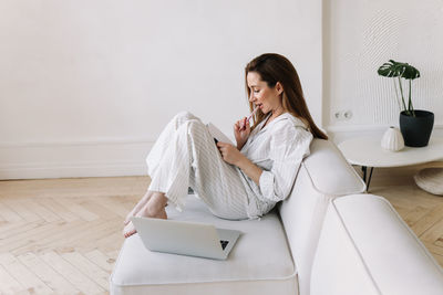 A business woman plans a day makes notes on a laptop while sitting on the couch at home