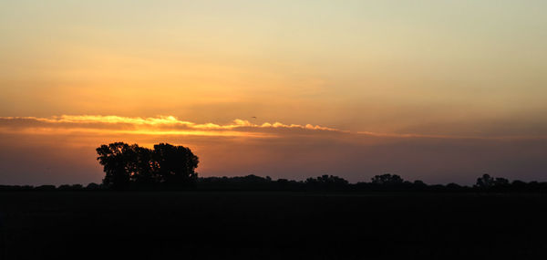 Silhouette trees on field against romantic sky at sunset