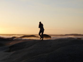 Silhouette man standing on beach against sky during sunset