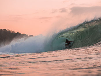 Man surfing in sea against sky during sunset