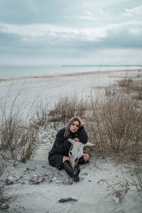 Full length of man sitting on shore at beach against sky