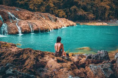 Rear view of woman sitting on rock by sea