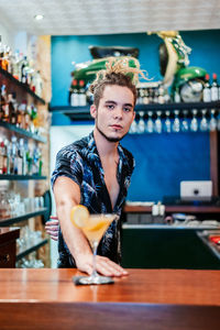 Serious barman pouring fresh alcohol cocktail in glass goblet placed on counter in bar