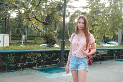 Portrait of beautiful young woman standing against trees