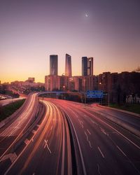 Light trails on road amidst buildings against sky at night