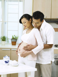 Smiling pregnant woman with man standing at home