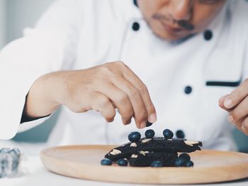 Midsection of chef garnishing berries on sweet food
