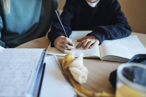 Midsection of boy doing homework in book sitting by mother at table