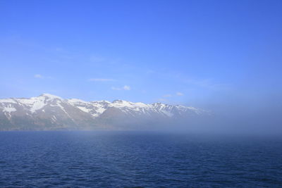 Scenic view of sea and snowcapped mountains against blue sky