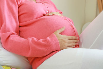 Midsection of pregnant woman sitting at home