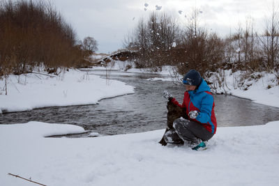 Woman playing with dog on snow by stream during winter