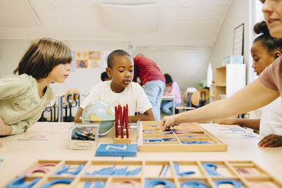 Students learning spellings at table by teacher in classroom