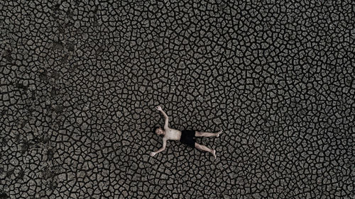 High angle view of shirtless boy with arms outstretched lying on cracked land