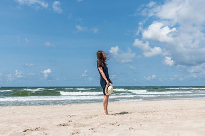 Rear view of woman standing at beach against sky