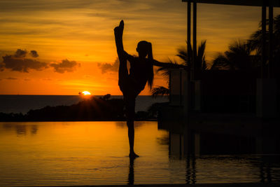 Silhouette woman with arms raised against orange sunset sky