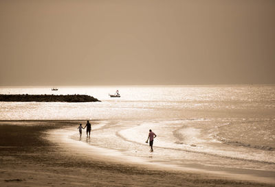 People on beach against clear sky during sunset