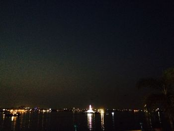 Illuminated cityscape by sea against sky at night