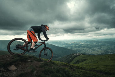 Man riding bicycle on mountain against sky