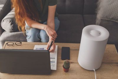 Midsection of woman writing in form by laptop at home