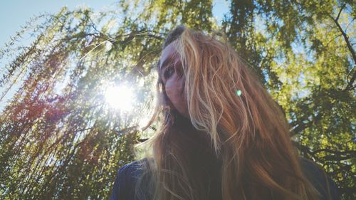 Low angle view of woman with blond hair against trees on sunny day