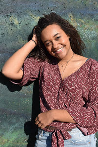 Portrait of smiling young woman standing against wall