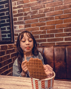 Full length of a girl sitting against brick wall