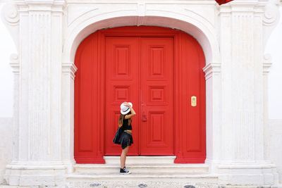 Side view of woman standing by closed red door