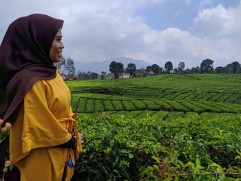 Smiling woman looking away while standing by plants against sky