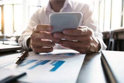Midsection of man using mobile phone on table