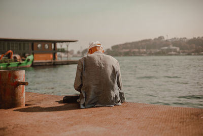 Rear view of man sitting on shore against sky