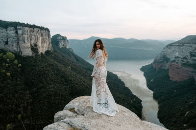 Woman standing on rock by mountain against sky